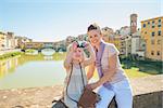 Mother and baby girl taking photo while standing on bridge overlooking ponte vecchio in florence, italy