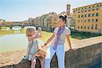 Baby girl taking photo of mother while sitting on bridge overlooking ponte vecchio in florence, italy