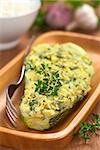 Baked zucchini stuffed with mashed potato, cheese and herbs (thyme, oregano, parsley, garlic) garnished with thyme served on wooden plate with a fork beside and a bowl of cooked rice in the back (Selective Focus, Focus on the front of the thyme garnish on the zucchini)