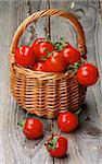 Arrangement of Perfect Ripe Cherry Tomatoes with Stems in Wicker Basket isolated on Rustic Wooden background