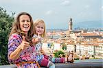 Happy mother and baby girl showing thumbs up against panoramic view of florence, italy
