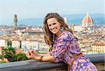 Happy young woman holding cell phone against panoramic view of florence, italy