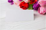 Colorful tulips and white card on wooden table