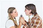 Happy geeky hipsters singing with microphone on white background