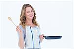 Smiling woman holding frying pan and wooden spoon on white background