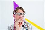 Geeky hipster wearing a party hat with blowing party horn on white background