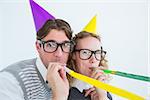 Geeky hipster couple blowing party horn on white background