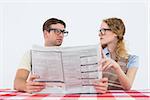 Geeky hipster couple reading newspaper on white background