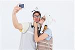 Geeky hipster couple taking selfie with smartphone on white background