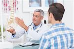 Doctor showing his patient a spine model in medical office