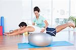Trainer with man on exercise ball in fitness studio