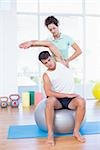 Man stretching his arm with trainer in fitness studio