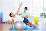 Trainer helping man with exercise ball in fitness studio