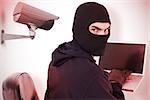 Hacker sitting and hacking laptop  against cctv camera