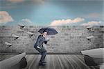 Businessman sheltering under black umbrella against blue sky over brick wall