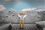 Geeky businessman holding paper bags against blue sky over brick wall