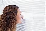 Curious woman looking through blinds in the house