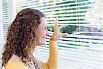 Curious woman looking through blinds in the house