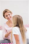 Mother brushing her daughters hair at home in the bedroom