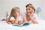 Mother and daughter reading book together on bed at home in the bedroom