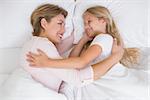 Mother and daughter cuddling in bed at home in the bedroom