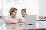 Mother and daughter using laptop at home in kitchen