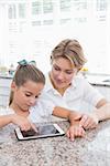 Mother and daughter using tablet pc at home in kitchen