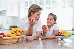 Mother and daughter holding apples at home in kitchen