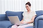 Casual brunette using laptop on couch at home in the living room