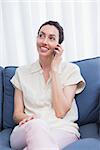 Casual brunette using phone on couch at home in the living room