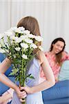 Daughter surprising mother with flowers at home in the living room