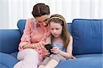 Mother and daughter using smartphone on couch at home in the living room