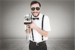 Geeky hipster holding a retro camera against grey room