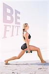 Fit blonde doing weighted lunges on the beach against be fit