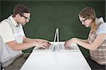 Geeky hipster couple using laptop against green chalkboard