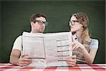 Geeky hipster couple reading newspaper against green chalkboard