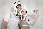 Geeky hipster couple taking selfie with smartphone against white background