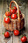 Heap of Perfect Ripe Cherry Tomatoes with Stems in Wicker Basket isolated on Rustic Wooden background