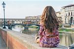 Young woman sitting near ponte vecchio in florence, italy. rear view