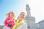 Happy mother and baby girl looking into distance in front of palazzo vecchio in florence, italy