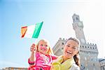 Portrait of happy mother and baby girl with flag in front of palazzo vecchio in florence, italy