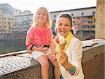 Closeup on smiling mother and baby girl showing ice cream near ponte vecchio in florence, italy