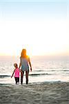 Healthy mother and baby girl walking on beach in the evening. rear view