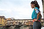 Thoughtful fitness woman standing in front of ponte vecchio in florence, italy