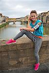 Full length portrait of happy fitness woman in earphones in front of ponte vecchio in florence, italy