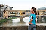 Smiling fitness woman standing in front of ponte vecchio in florence, italy. rear view