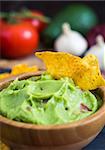 Guacamole in Wooden Bowl with Tortilla Chips and Ingredients Close Up