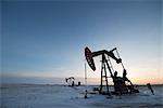 An oil drilling rig and pumpjack on a flat plain in the Canadian oil fields at sunset.