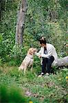 A woman seated on a log patting her retriever dog.