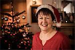 A woman by a Christmas tree wearing a Santa hat.